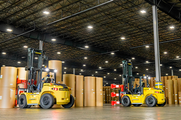 Two Hyster ® trucks with custom Bolzoni attachments lift paper bales in a warehouse